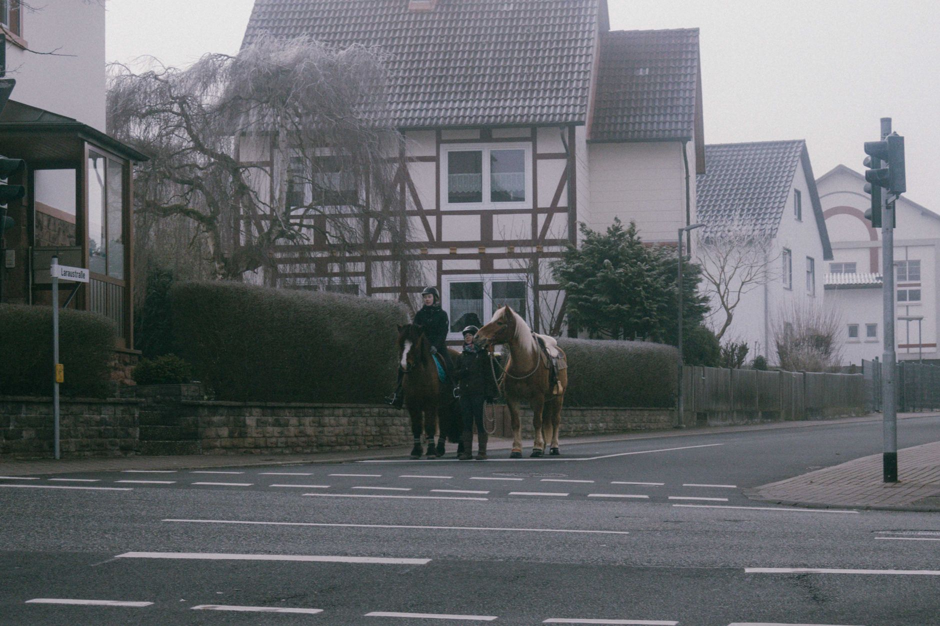 Two riders on horses cross a foggy street near traditional half-timbered houses.