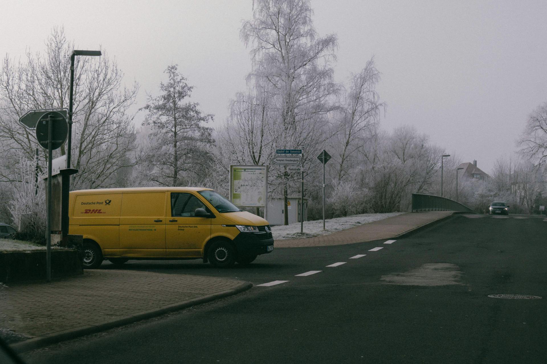 A yellow DHL delivery van parked on a frosty winter street corner, showcasing urban logistics.