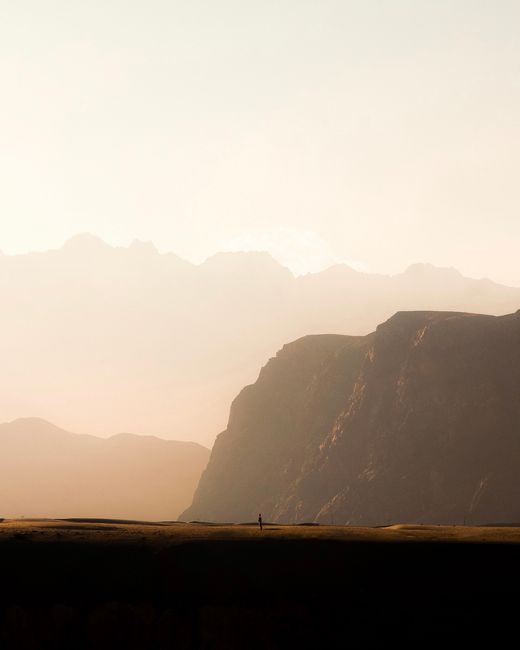 Single person in vast landscape with towering cliffs and golden light.