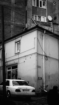 Monochrome urban street view with buildings and parked car, capturing an everyday city moment.