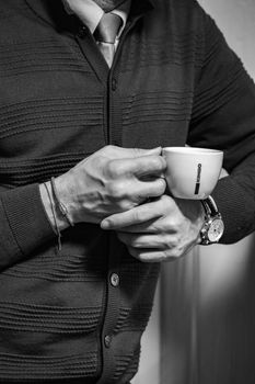 Closeup black and white image of a man holding a coffee cup in formal attire, highlighting lifestyle elegance.