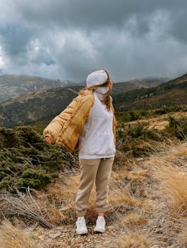 Person in warm clothing enjoys hiking in rugged mountain landscape under cloudy skies.