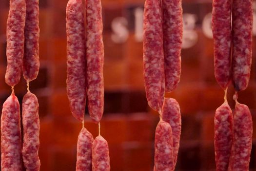 Close-up of hanging cured sausages in a traditional butcher shop setting.