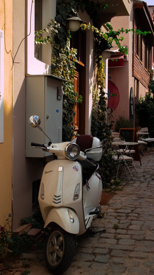 Free Vintage scooter parked in an ivy-covered alleyway with outdoor seating, creating a quaint street view. Stock Photo