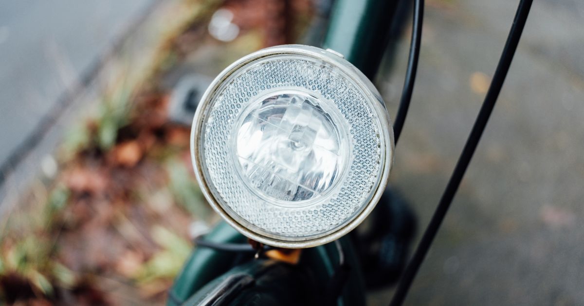 A chrome bike headlamp on the handlebars of a green bike