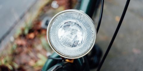 A chrome bike headlamp on the handlebars of a green bike
