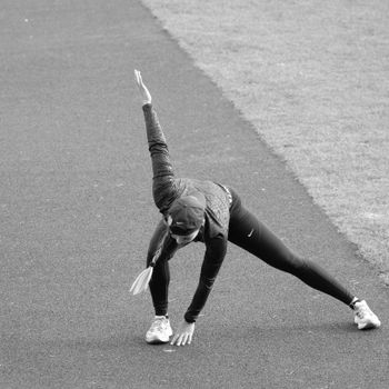 Athletic woman performs warm-up exercise on track. Black and white photo.