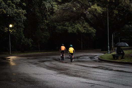 Two cyclists riding through a wet park in São Paulo under dim light, capturing a peaceful rainy day scene.