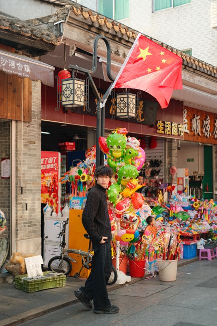 Fotomural Escena callejera vibrante con bandera china y exhibición de juguetes coloridos, atmósfera animada.