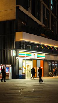 City street scene at night with people outside a brightly lit convenience store.
