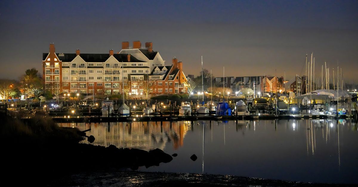Scenic view of Stamford marina with office buildings and sailboats at twilight.