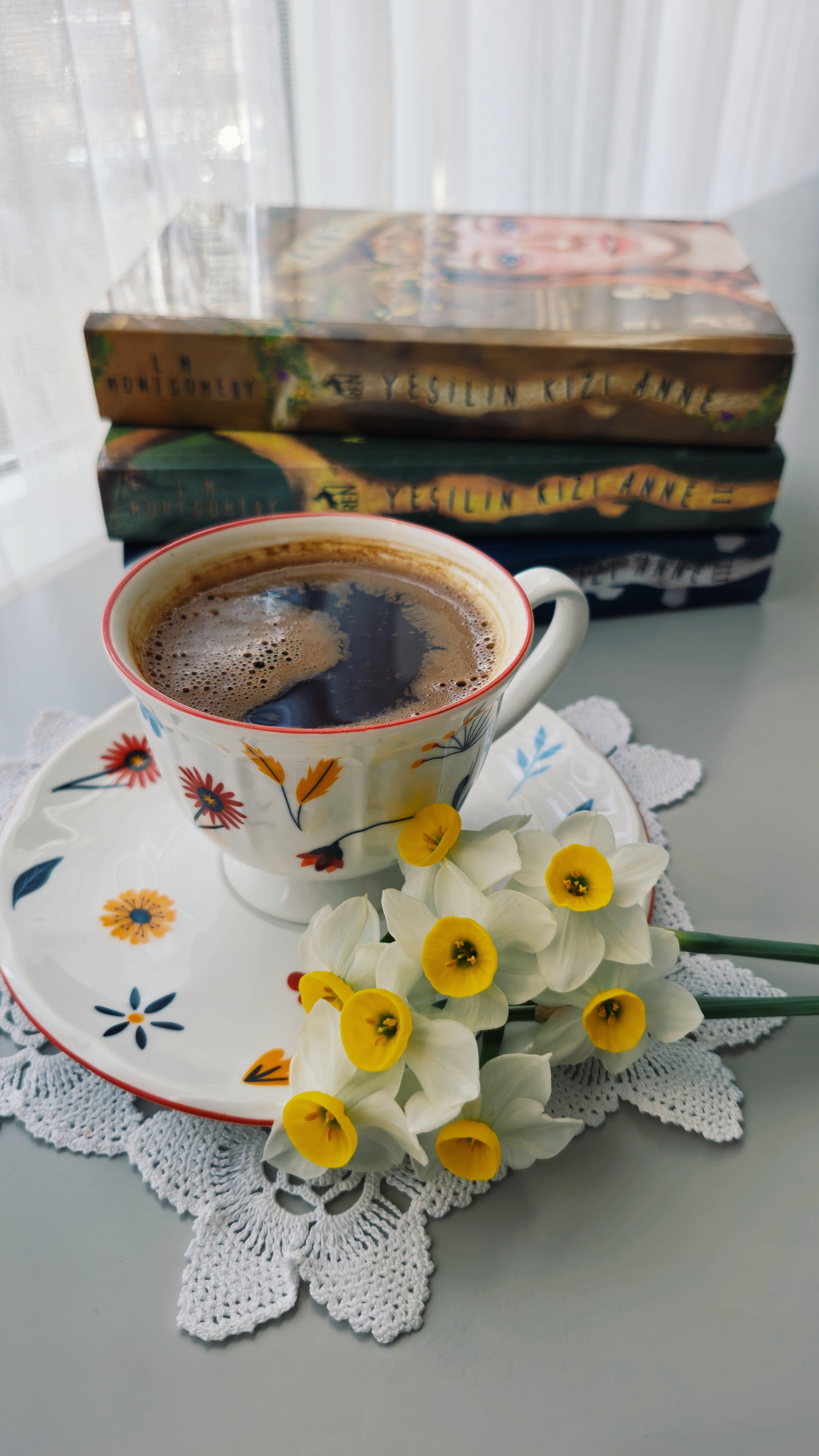 Aesthetic coffee cup with flowers beside books on a table, perfect for cozy vibes.