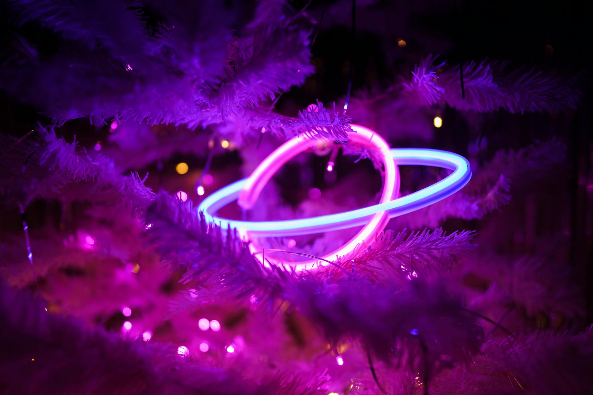 A glowing neon planet ornament nested among purple Christmas tree branches, creating a festive and futuristic vibe.