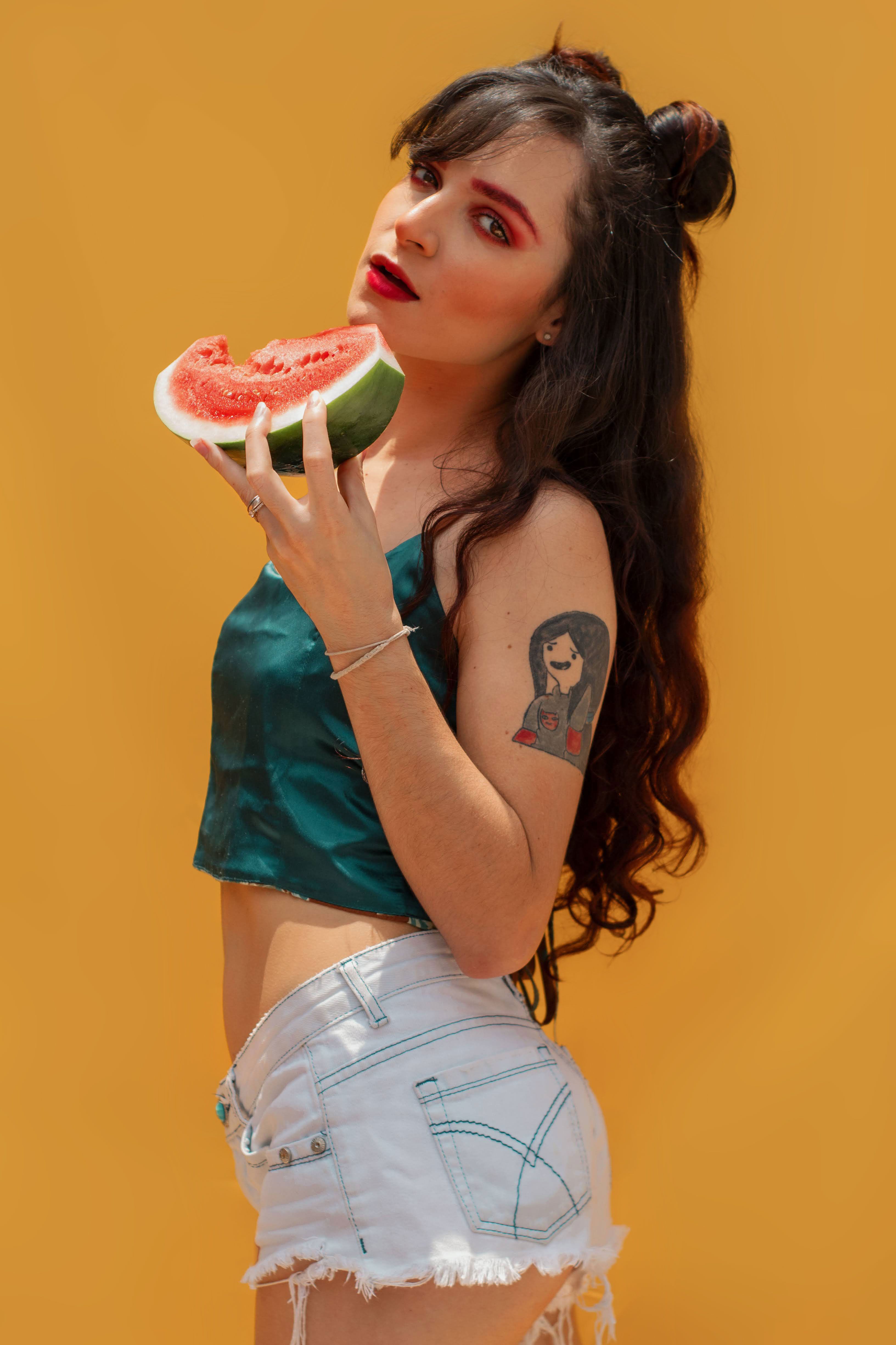 Vibrant portrait of a woman enjoying watermelon against a yellow backdrop in São Paulo, Brazil.