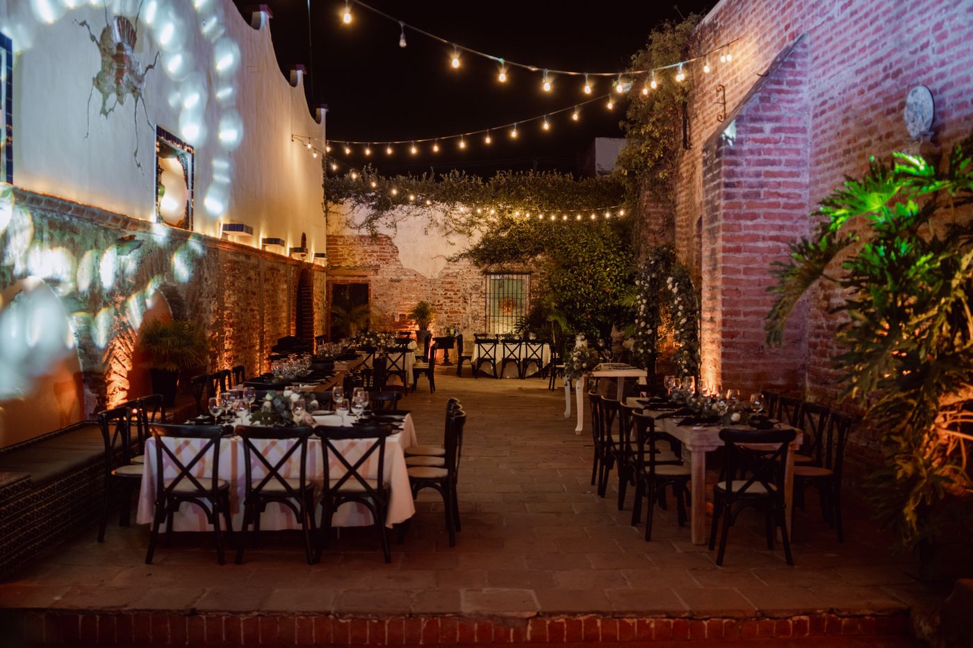 Old brick courtyard laid for a night reception under bulb strings — representative image