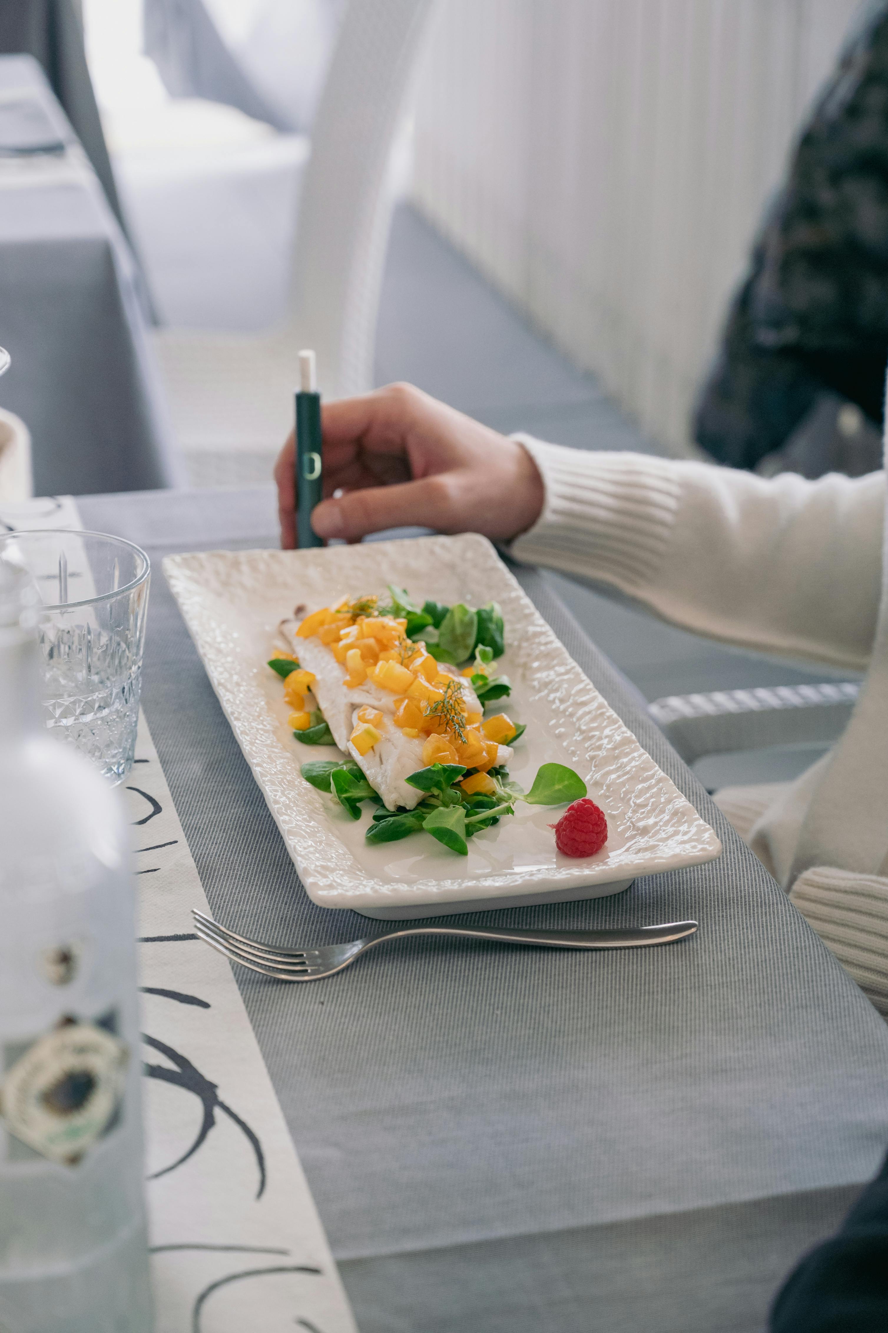 Elegant seafood dish with greens and raspberry garnish in Italian restaurant setting.