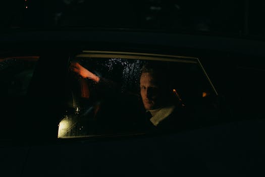 A mysterious man gazes through a rainy car window in low light.
