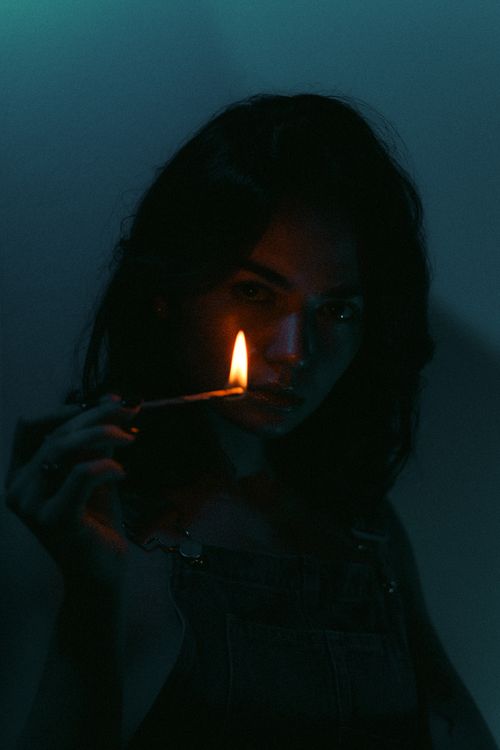 Free A dramatic, dark portrait of a woman holding a lit match in a shadowy setting. Stock Photo