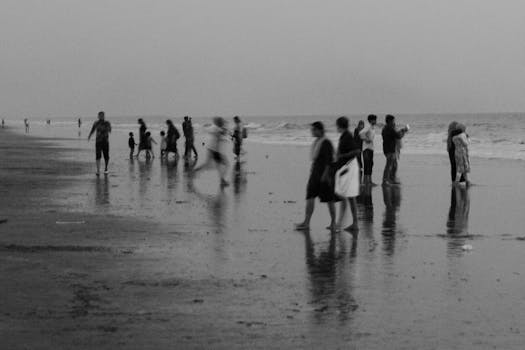 A black and white photo capturing blurred people walking along a beach shoreline.
