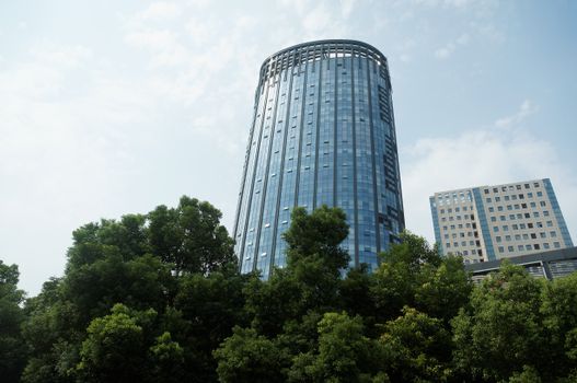 A modern skyscraper rises above lush greenery, showcasing urban architecture against a clear sky.