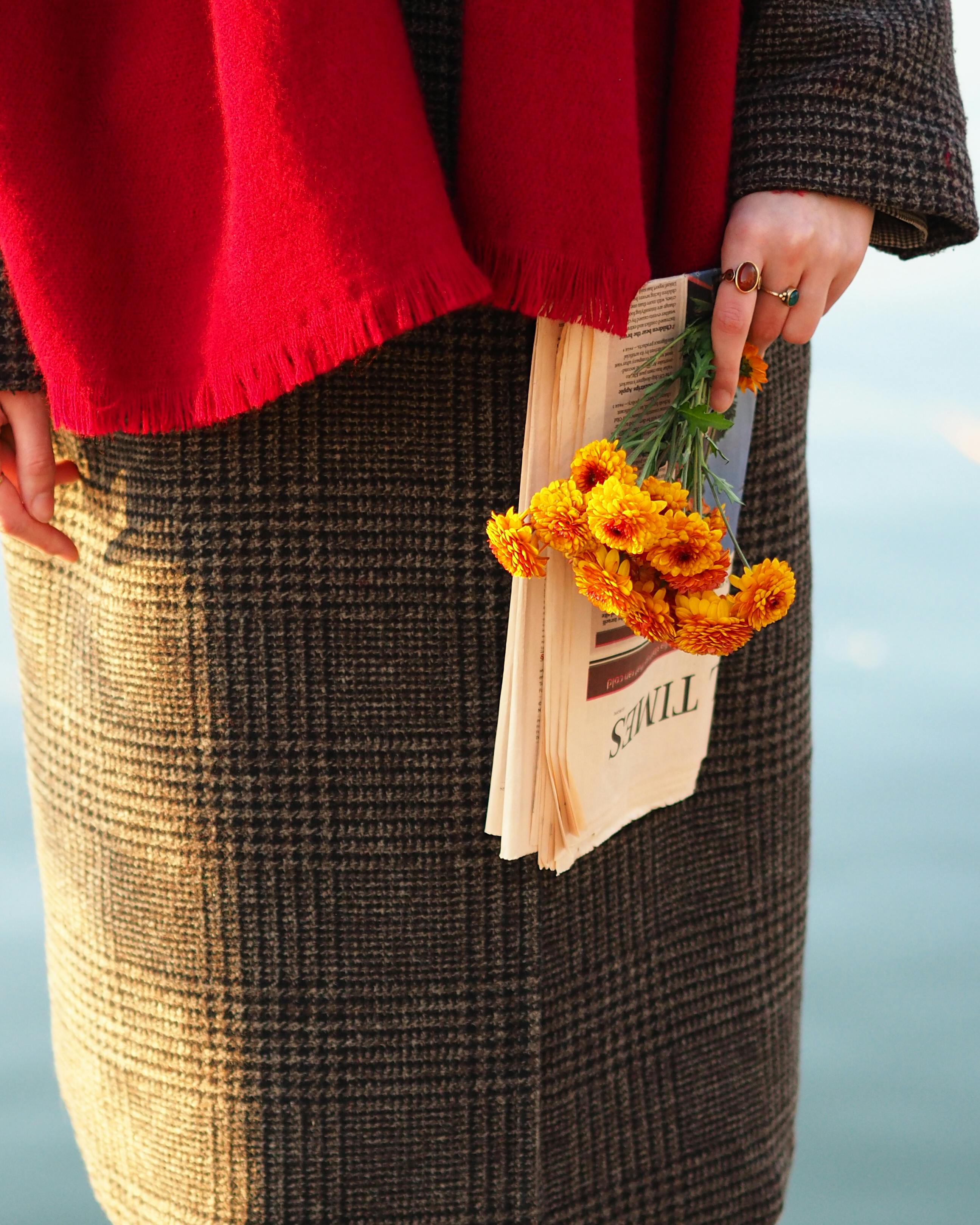 Chic autumn style with a red scarf, plaid coat, and bright flowers.