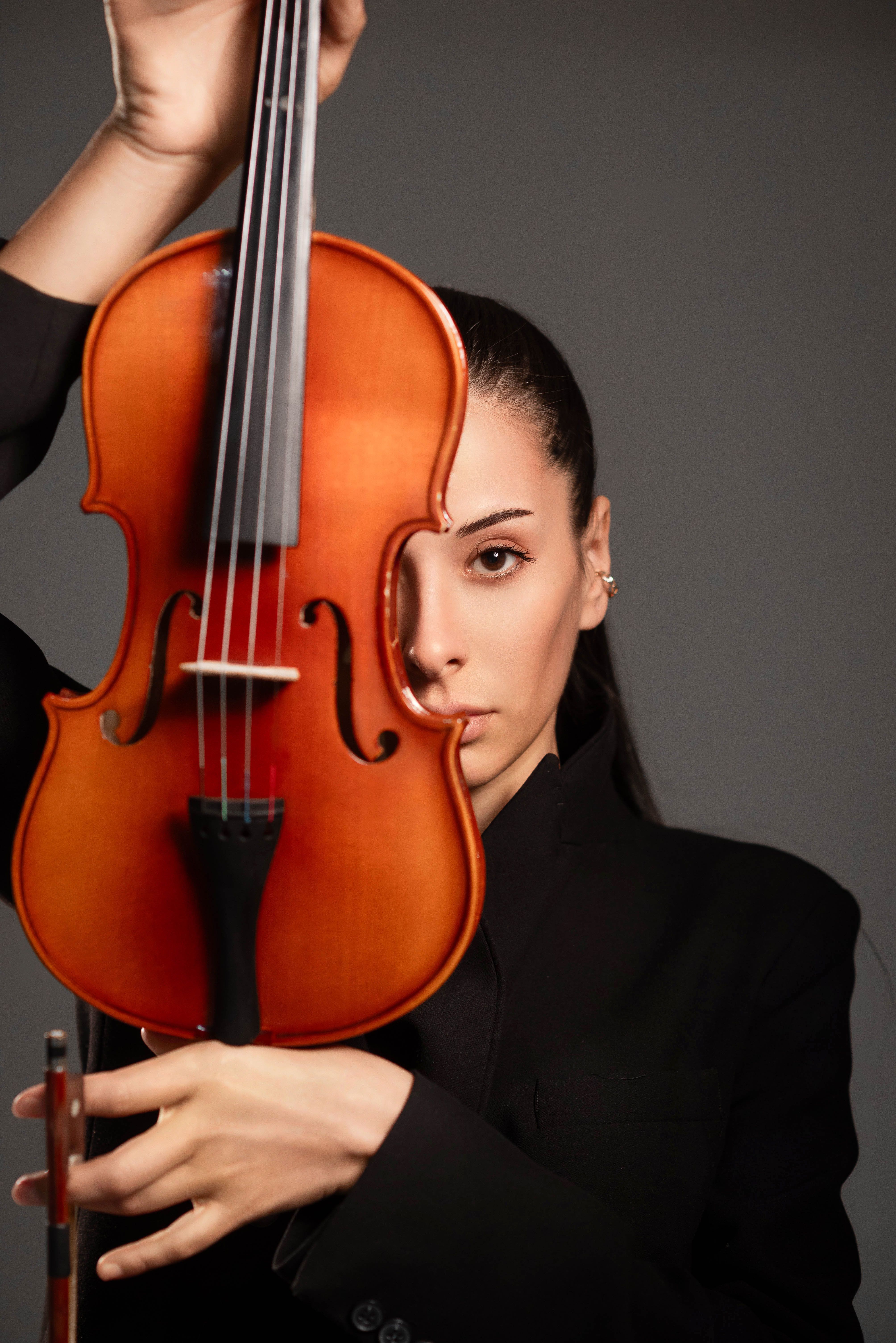 A poised female violinist elegantly holding a violin in a studio setting.