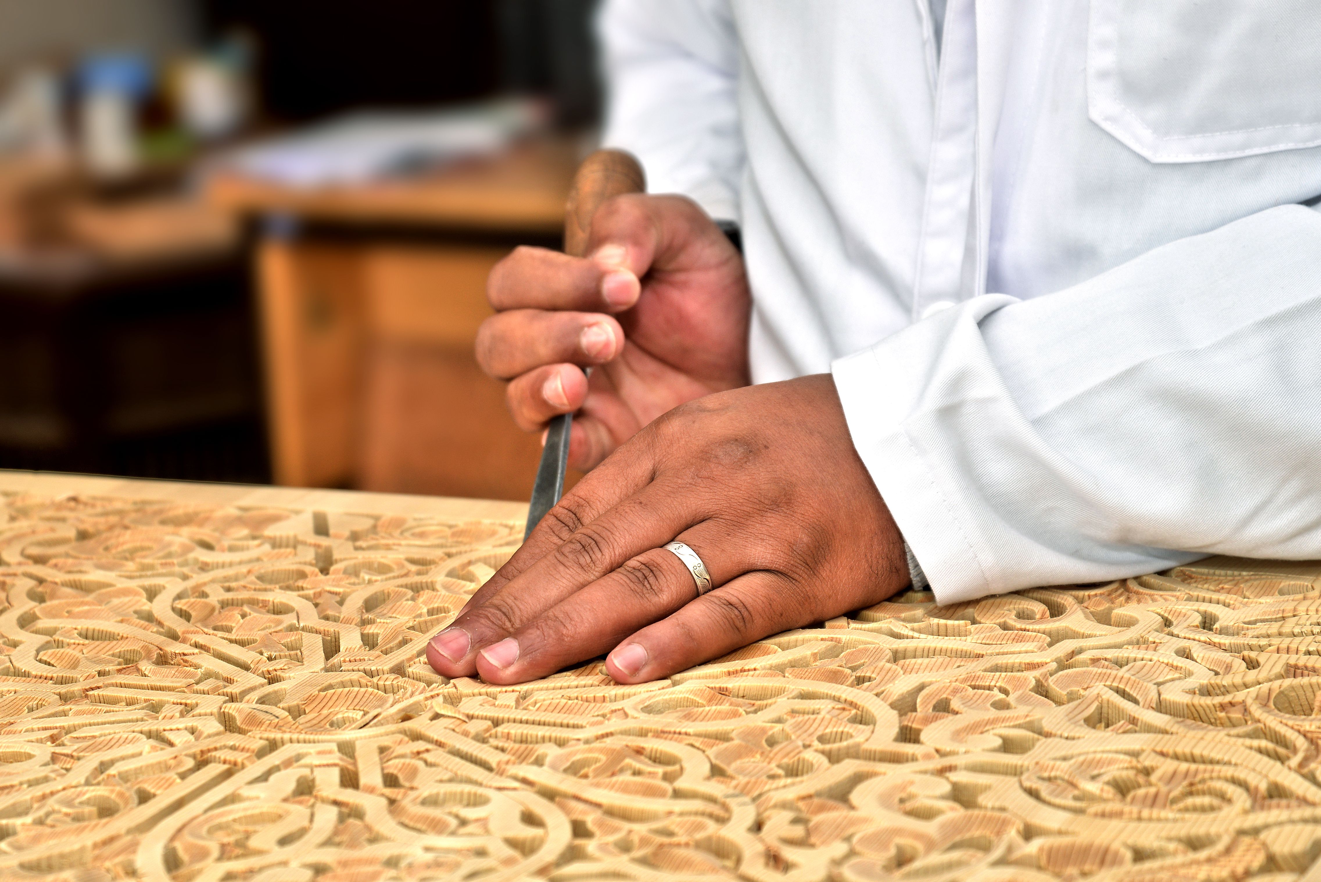 Close-up of an artisan's hands skillfully carving wood in a traditional Moroccan workshop.
