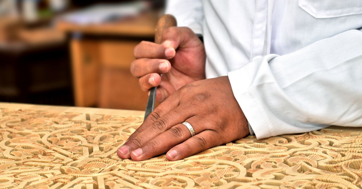 Close-up of an artisan's hands skillfully carving wood in a traditional Moroccan workshop.