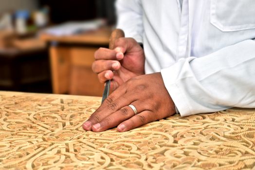 Close-up of an artisan's hands skillfully carving wood in a traditional Moroccan workshop.