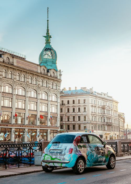 Free Urban scene with a colorful car, historic buildings, and clear blue sky, capturing city life. Stock Photo
