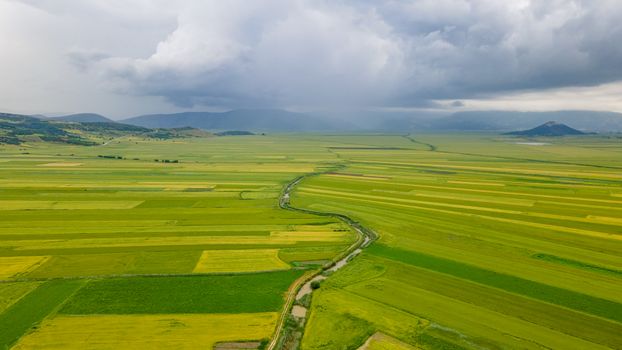 Aerial view of vast green fields under a dramatic sky in Çeltikçi, Türkiye.