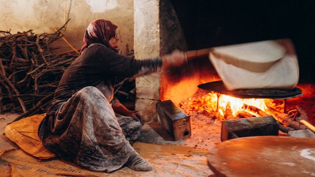 A woman baking traditional flatbread in a wood-fired oven in Çeltikçi, Türkiye.