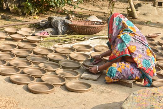 An artisan in colorful attire handcrafting clay pottery outdoors in Dhaka.