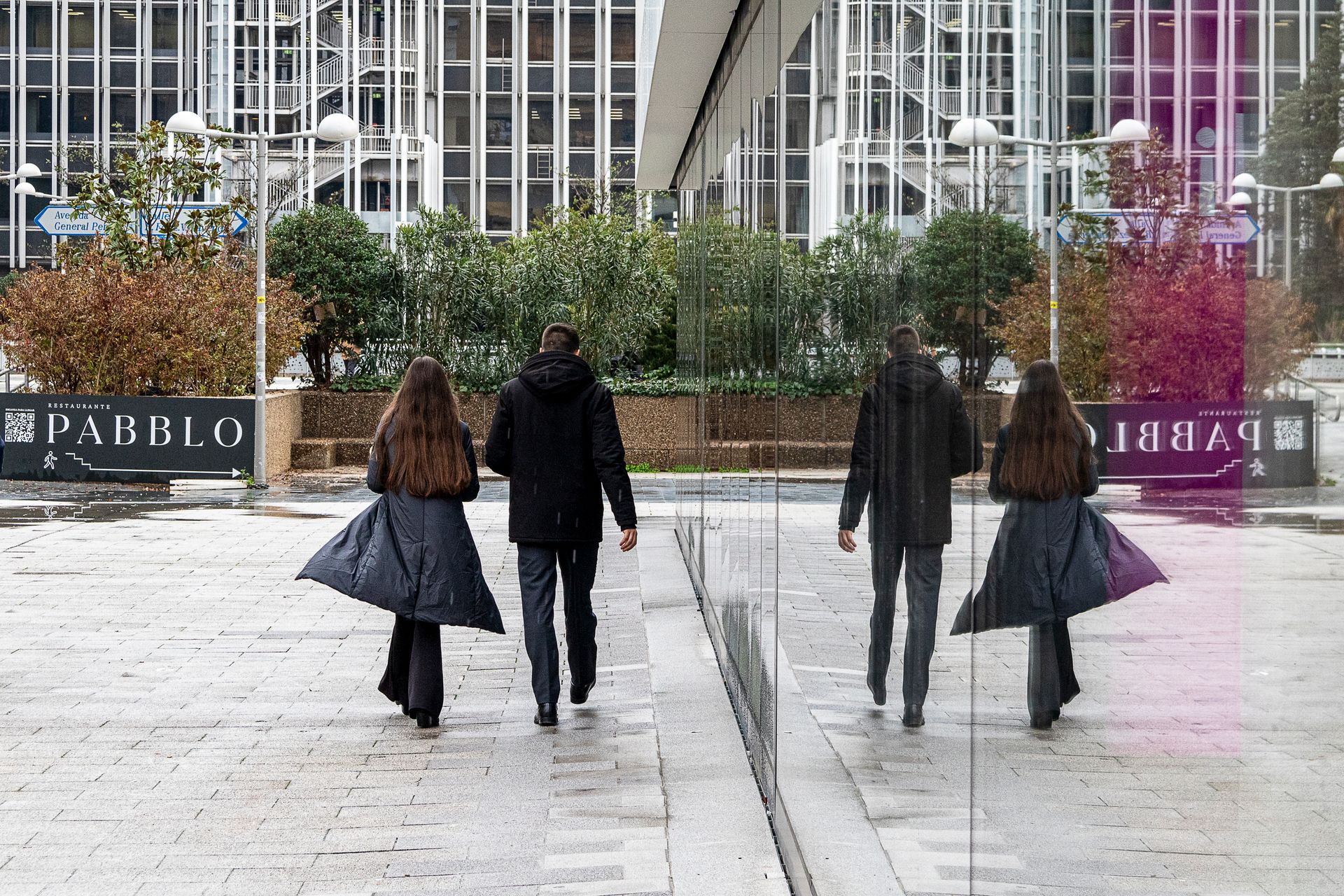Two people walking in Madrid with reflections in glass, showcasing urban architecture and modern design.