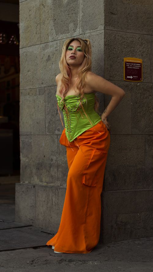 Free Stylish woman in vibrant outfit leaning against wall in urban setting, exuding confidence. Stock Photo
