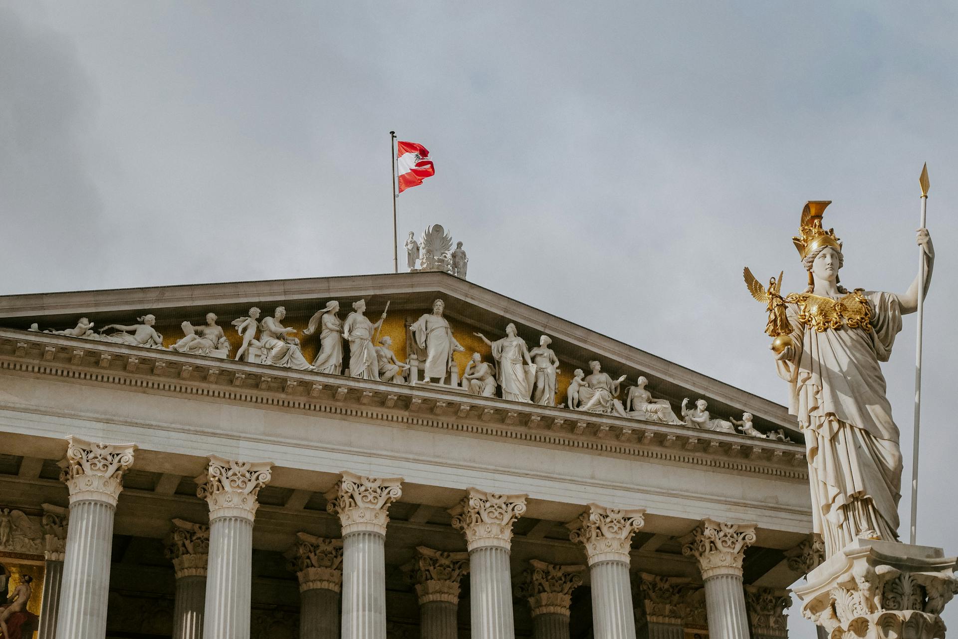 Front view of Austrian Parliament Building with Athena statue and national flag.