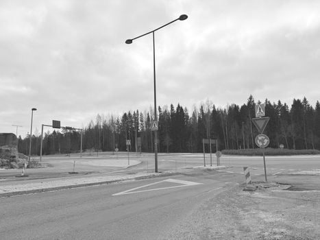 Black and white image of an empty roundabout with traffic signs and trees in the background.