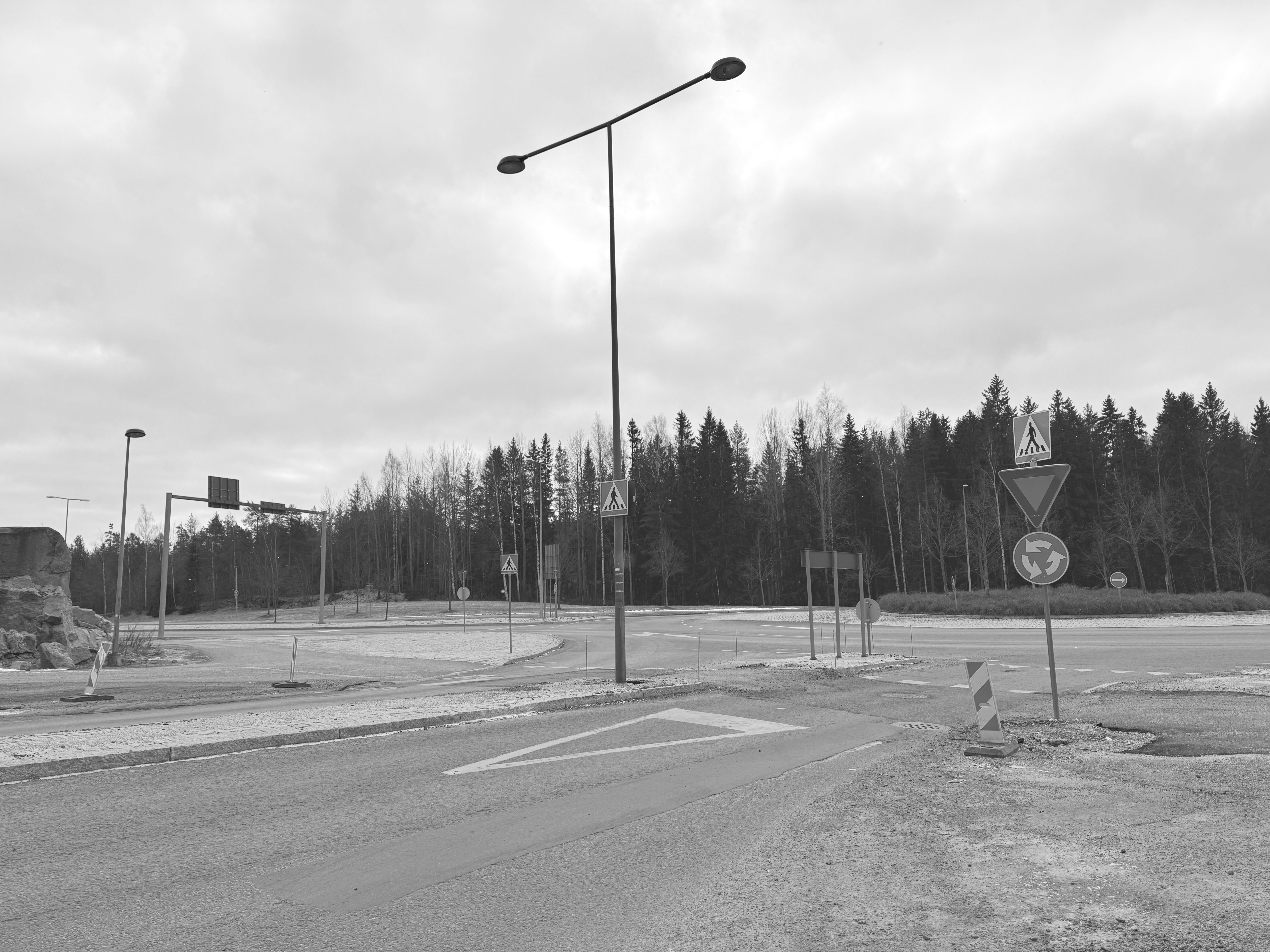 Gratis Sort/hvid billede af en tom rundkørsel med trafikskilte og træer i baggrunden. Lagerfoto
