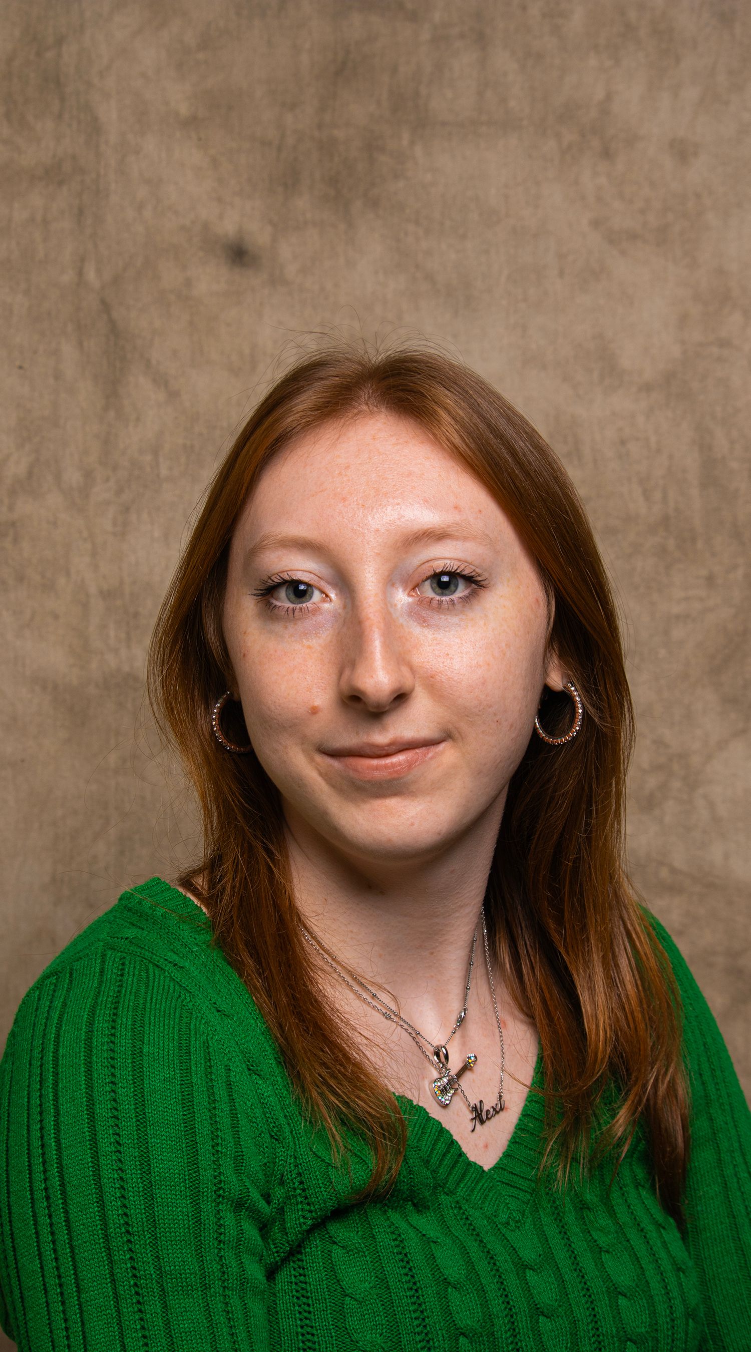 Elegant studio portrait of a young woman with red hair wearing a green sweater and jewelry.