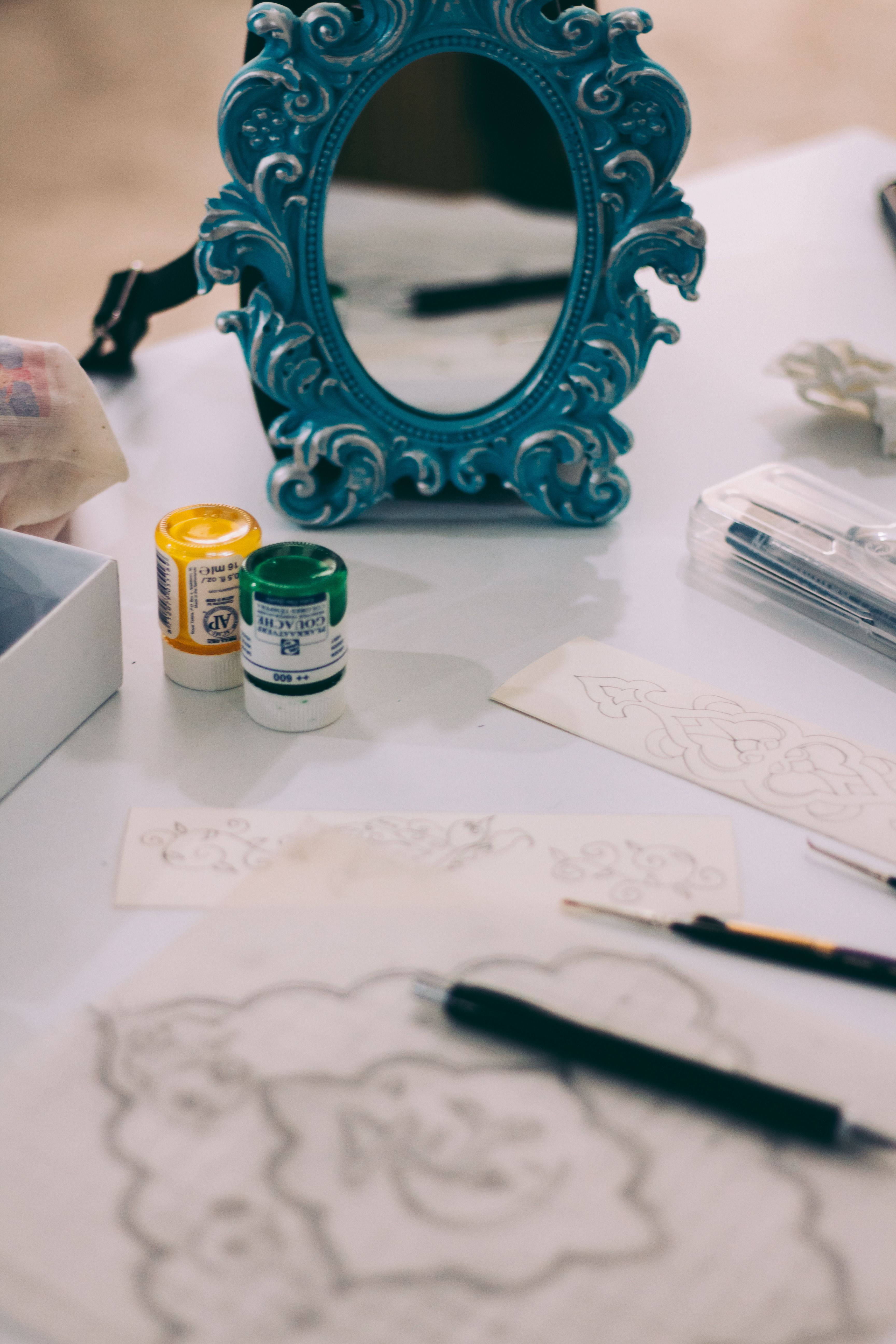 Flat lay of art supplies and blue ornate mirror on a table.