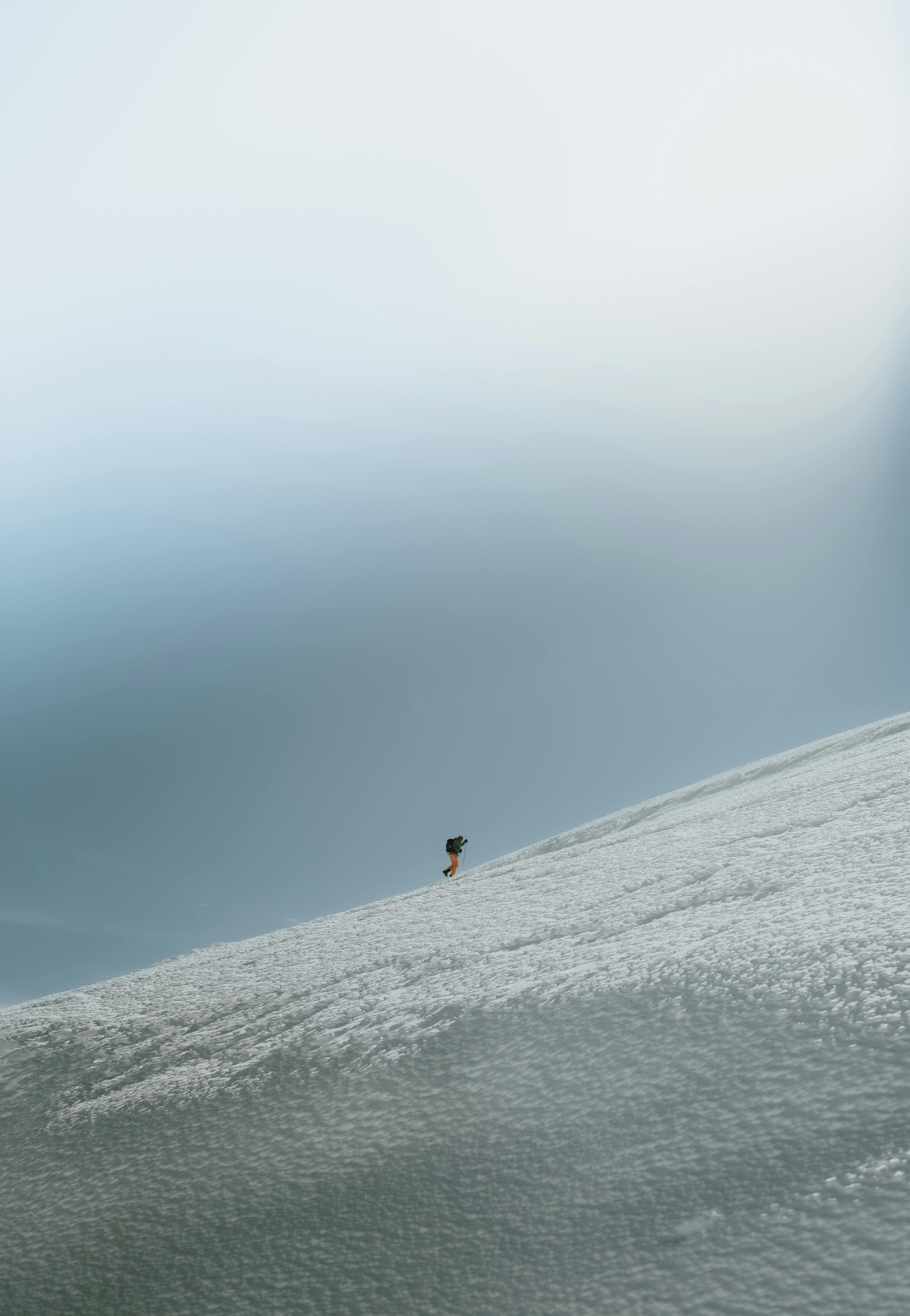 A solitary snowboarder descends a vast snowy slope under a clear blue sky, capturing winter adventure.