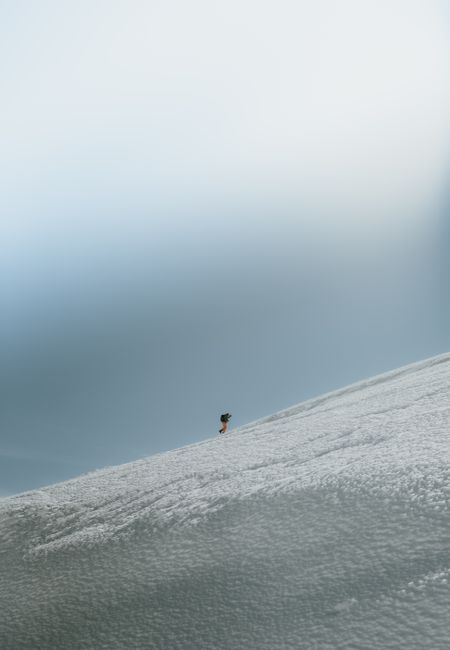 A solitary snowboarder descends a vast snowy slope under a clear blue sky, capturing winter adventure.