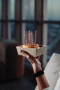 A slice of birthday cake with lit candles held by a person indoors, creating a celebratory mood.