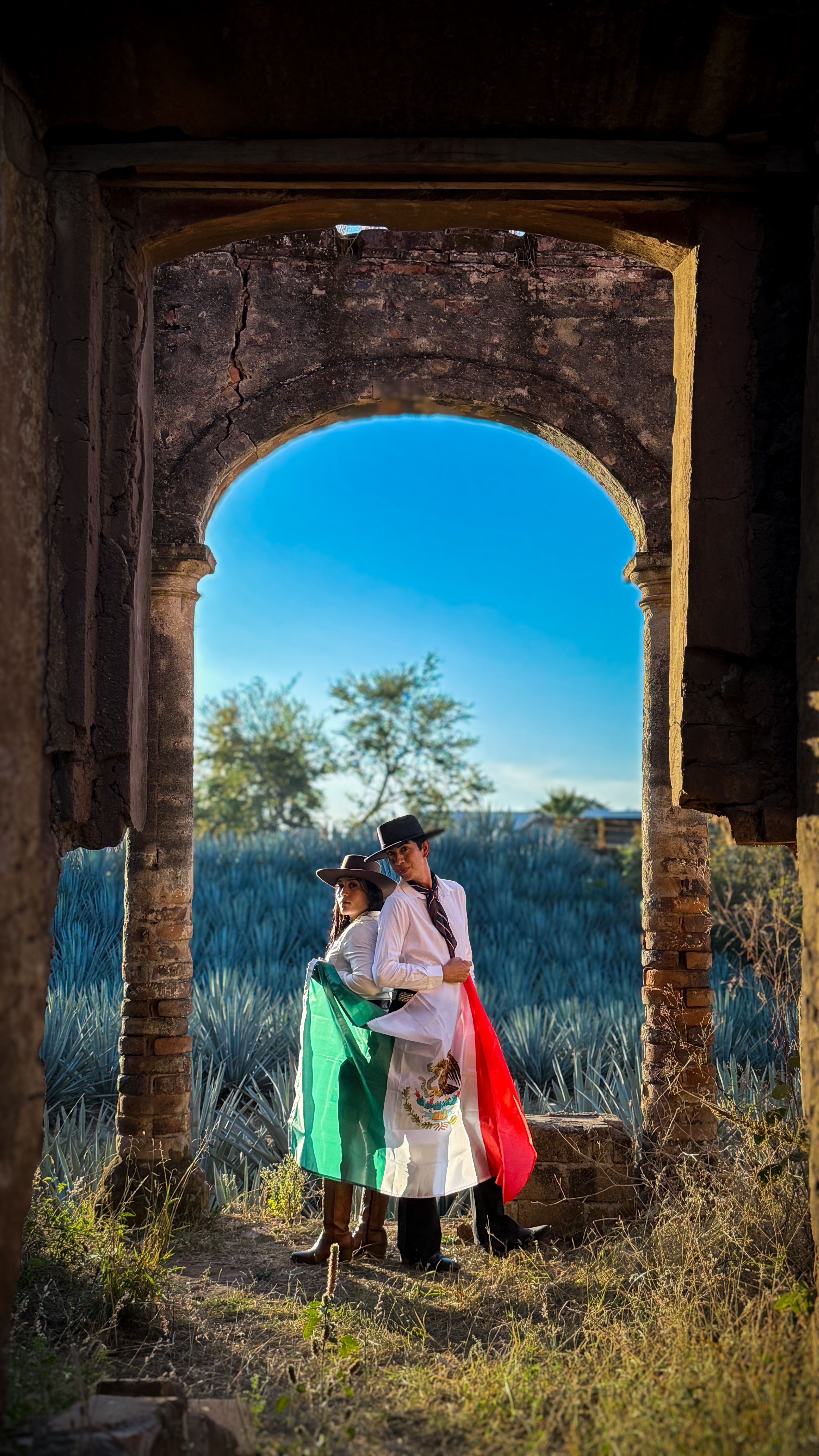 Two people with Mexican flag under ancient arch in Amatitán, Jalisco.