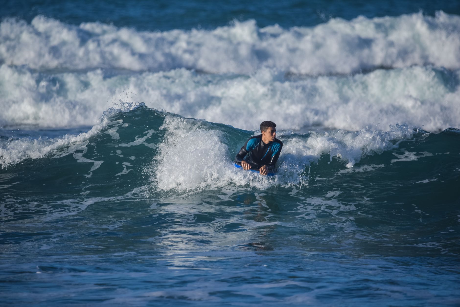 Man in blue wetsuit surfing on strong ocean waves during daytime.
