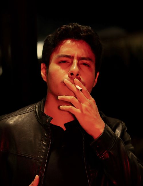 Free Moody portrait of a man smoking, wearing leather jacket in low light. Stock Photo