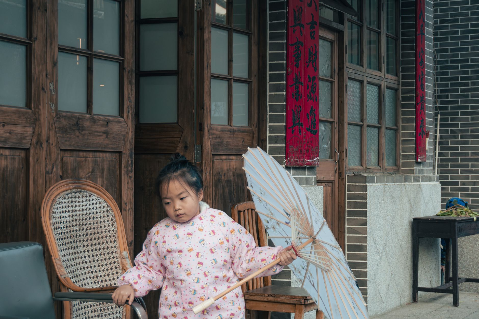 A young girl holding an umbrella outside a traditional Chinese home, hinting at cultural festivities.