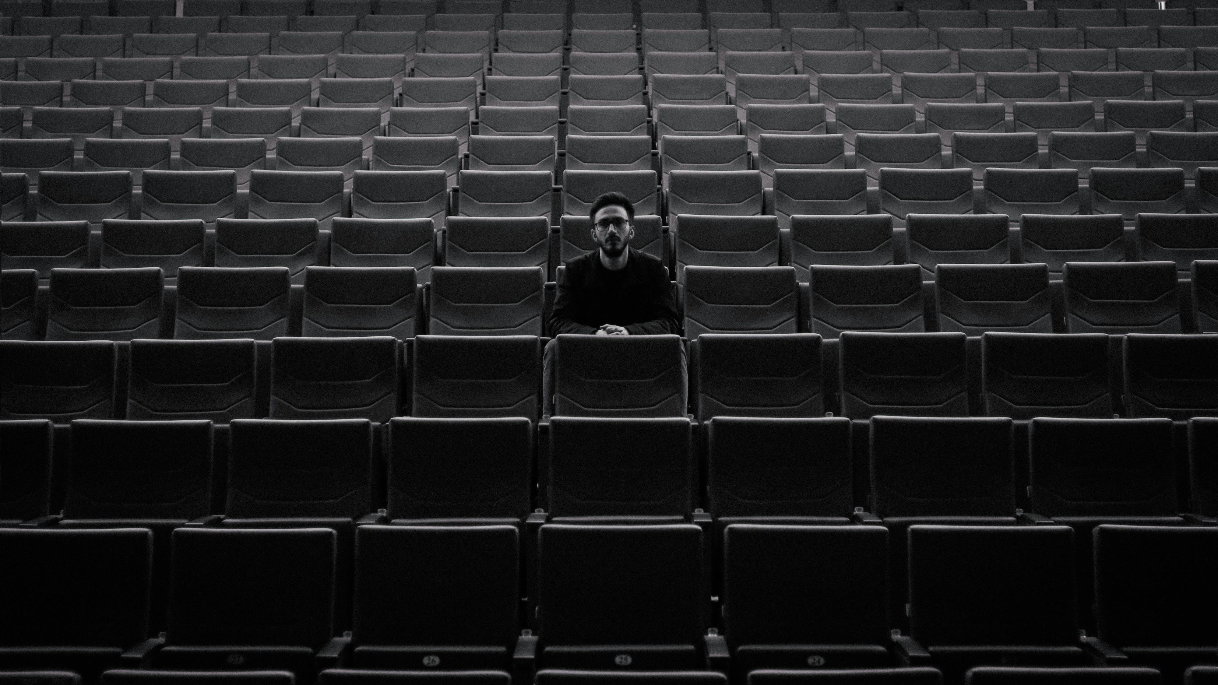 De franc Un individu solitari s'asseu entre fileres de seients buits del teatre, creant una atmosfera de mal humor. Foto d'estoc