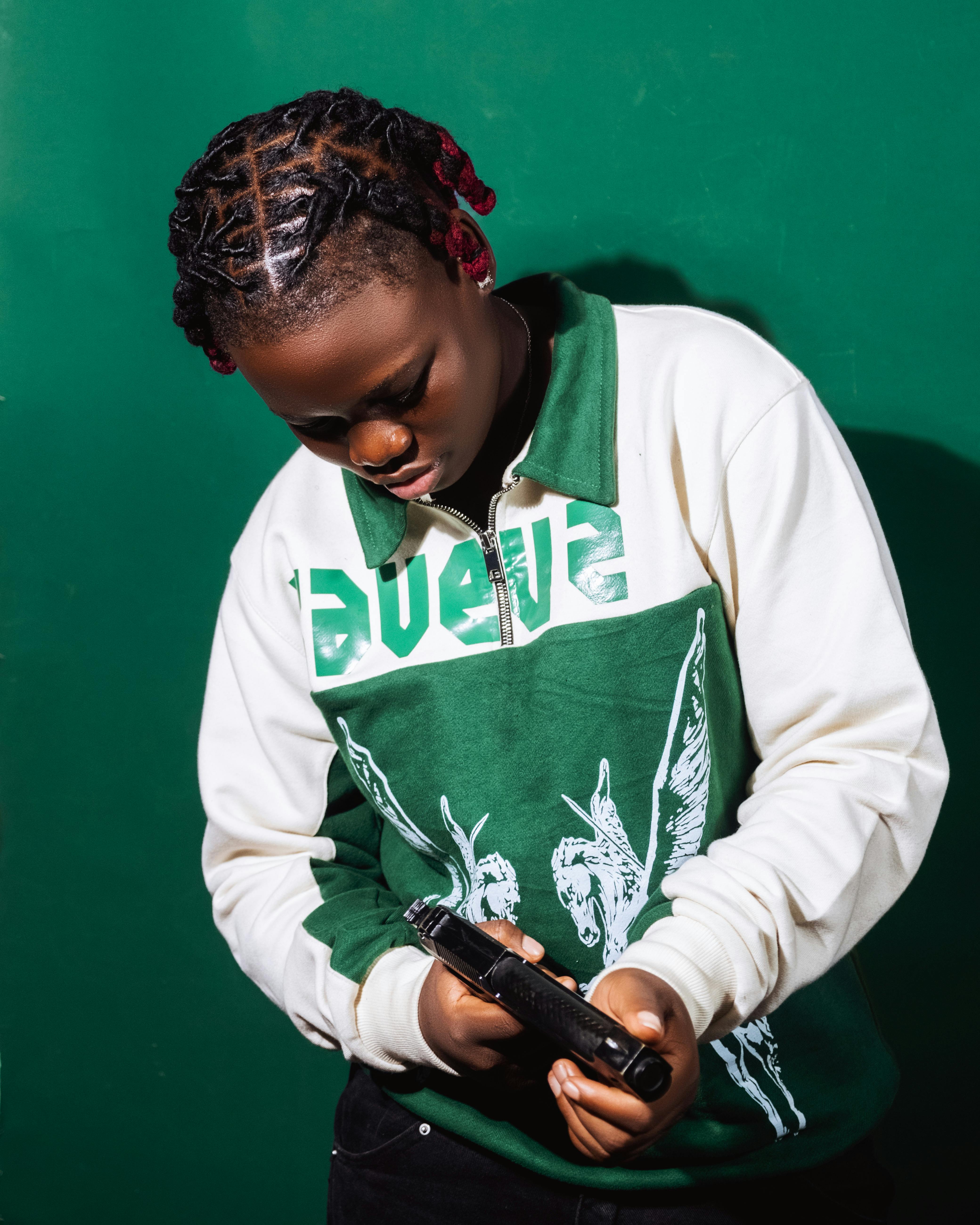 grátis Pessoa com cabelo trançado examinando um item contra um fundo verde. Foto profissional