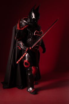 Intricately detailed superhero cosplay armor with sword against red backdrop.